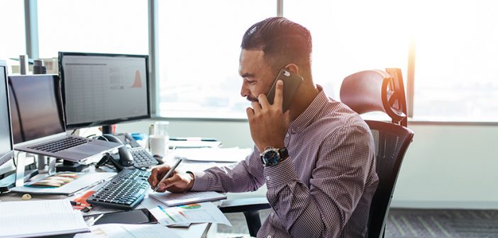 Businessman talking on mobile phone and making notes. Man sitting at his office desk working on graphs and charts and discussing on phone.