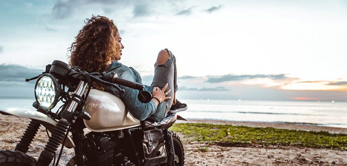 Beautiful girl having fun driving her motorcycle, enjoying the sunset on the beach