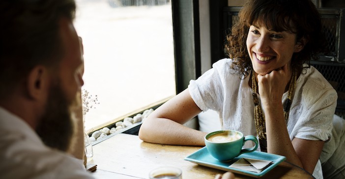 two people sitting in a cafe at a table drinking coffee smiling