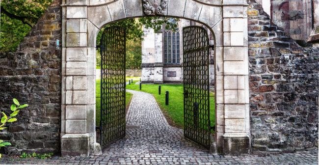 gray stone gateway to property leading to courtyard with green grass and gray brick pathway