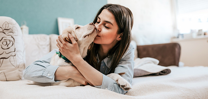 woman laying on bed snuggling light colored big dog