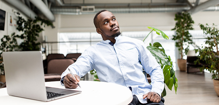 Pensive African man sitting in the office at the table making notes in a notebook