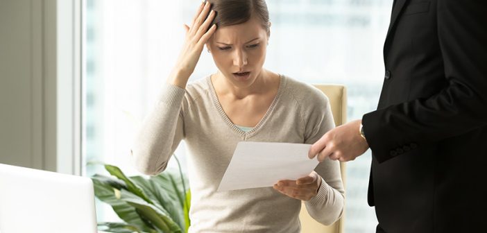 Puzzled businesswoman being presented lawsuit paperwork at desk in office 