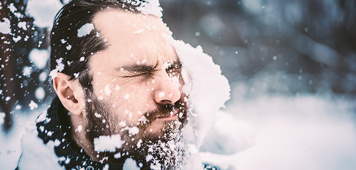 dark-haired bearded man getting hit in the face with a large snowball outside during winter